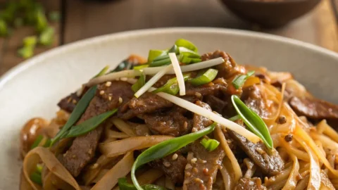 Bowl of Beef Chow Fun with wide noodles, tender beef, bean sprouts, and scallions in savory sauce.